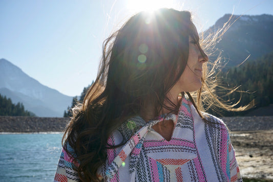 Woman in the sunlight wearing a mexican drug rug hoodie next to a mountain lake